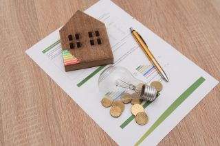 © Renata Hamuda - stock.adobe.com Foto: Glühbirne, Energieskala auf Haus, Münzen
